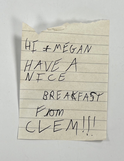 A yellow lined piece of paper with the words in capital letters: HI MEGAN HAVE A NICE BREAKFAST FROM CLEM!!!